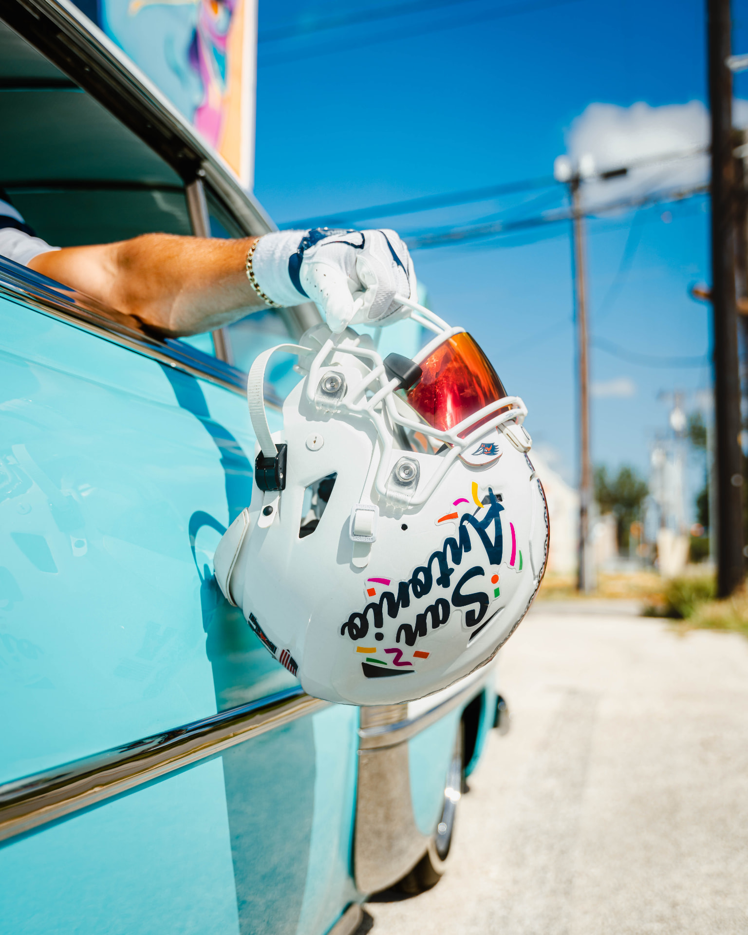 White UTSA San Antonio helmet held beside a turquoise car